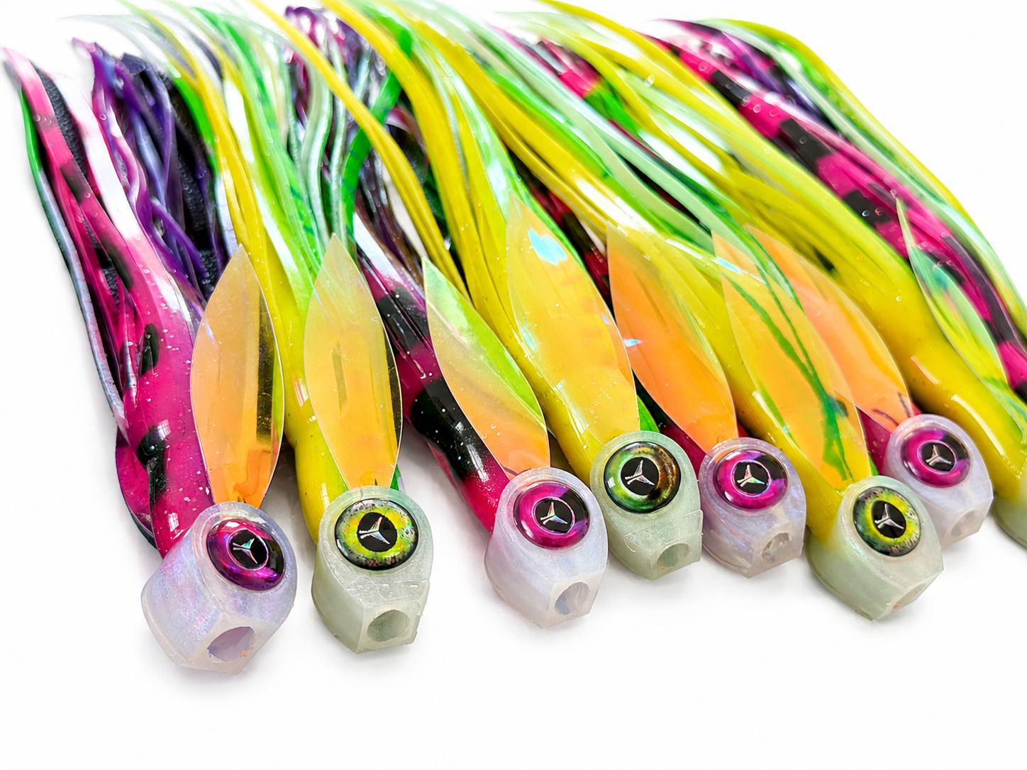 Six plastic fishing skirt jigs with colorful swirled tails and bead heads, arranged diagonally on a white background.