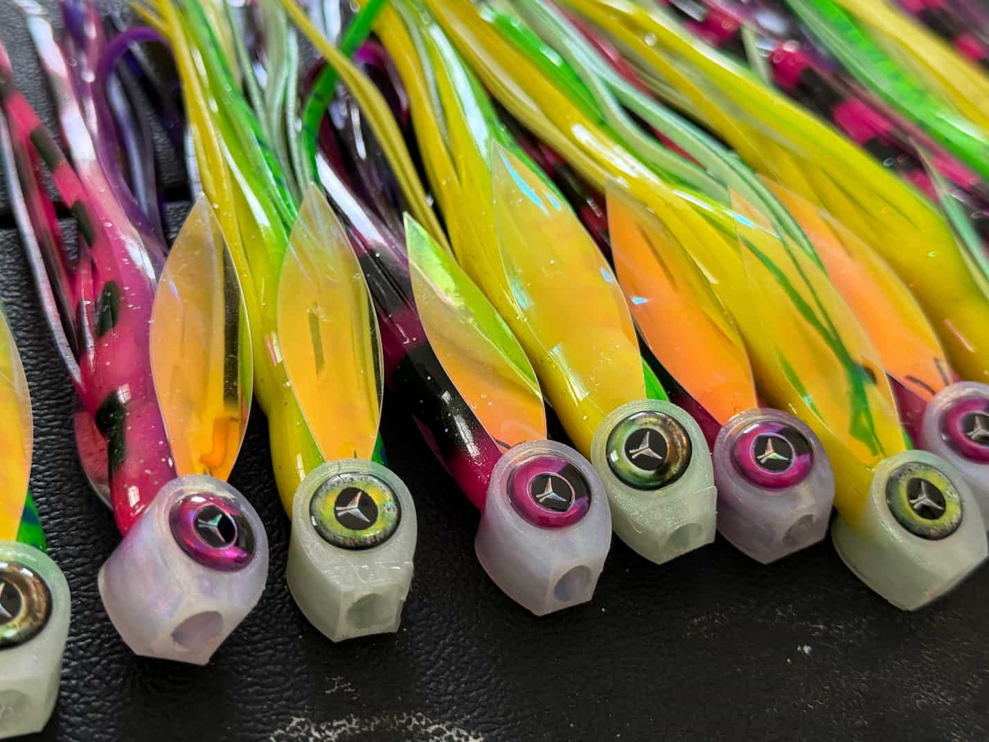 A close-up of several Abacoa Design offshore fishing lures The Hornet. The lures have translucent yellow and orange bodies with green, pink, and purple skirt strands, and translucent heads with custom eyes